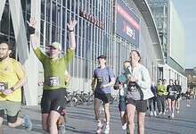 Runners in colorful athletic gear celebrating as they finish a race outside a modern venue, with other participants and spectators nearby.