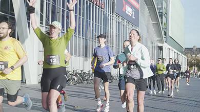 Runners in colorful athletic gear celebrating as they finish a race outside a modern venue, with other participants and spectators nearby.