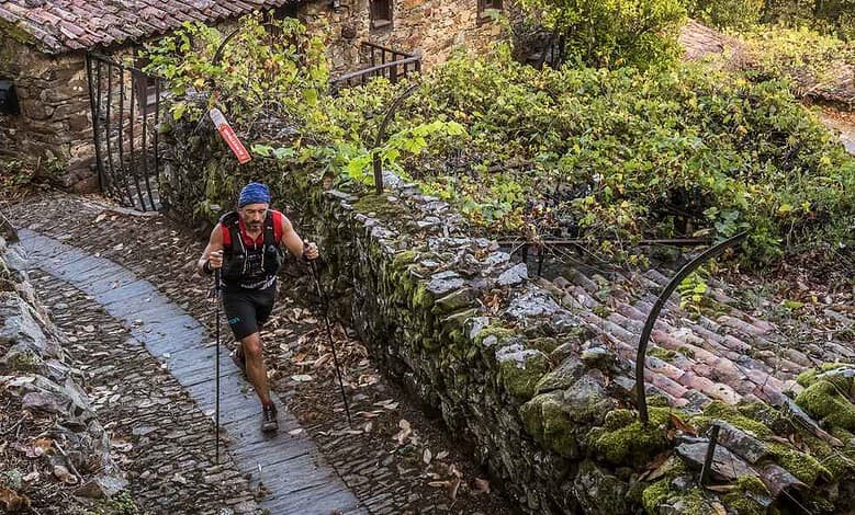 Male trail runner navigating a muddy path through a lush, green forested area with stone walls and rustic surroundings.