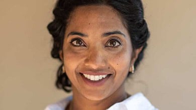 Portrait of a smiling woman in a white shirt, looking at the camera, on a neutral beige background, representing running insights and health analytics.