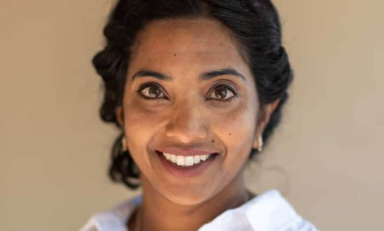 Portrait of a smiling woman in a white shirt, looking at the camera, on a neutral beige background, representing running insights and health analytics.