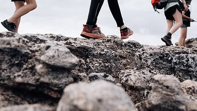 Runners crossing rugged rocky terrain during a trail race, focus on hiking shoes and uneven ground.