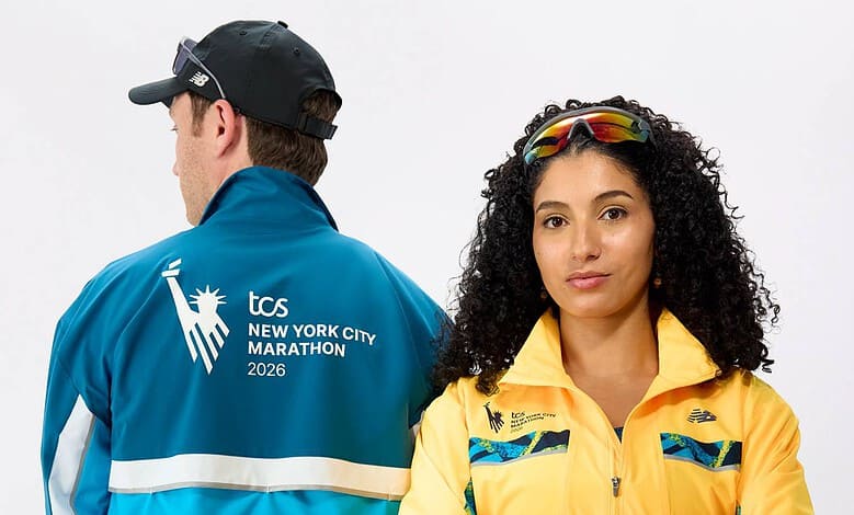Two runners pose for a studio shot: a man in a blue jacket with TCS New York City Marathon 2026 logo on the back, and a woman in a yellow jacket with reflective sunglasses on her head, against a white.