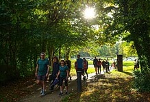 A group of runners jogging through a lush green park with sunlight filtering through trees, promoting outdoor running and fitness.