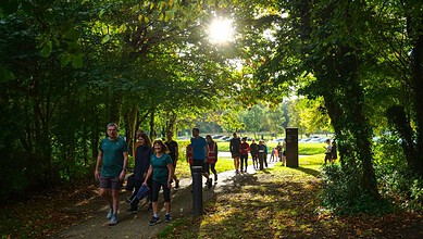 A group of runners jogging through a lush green park with sunlight filtering through trees, promoting outdoor running and fitness.