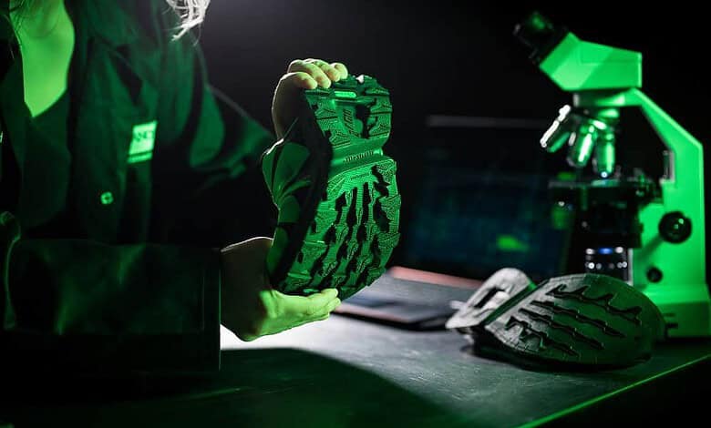 Person inspecting a shoe sole under green lab lighting with a microscope and lab bench setup, highlighting performance footwear details for running insights.