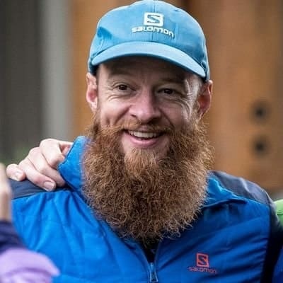 Smiling bearded man in a blue outdoor jacket and blue cap with Salomon logo, representing Running Insights.