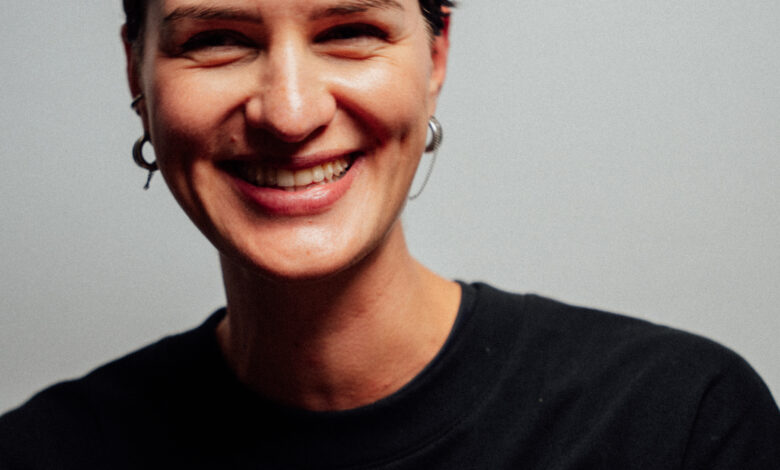 Smiling female runner with short dark hair wearing a black running shirt, showcasing confidence and fitness, against a plain grey background.