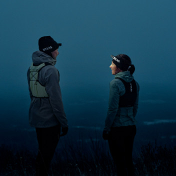 Two runners in trail running gear talking outdoors during dusk, highlighting outdoor running and fitness.