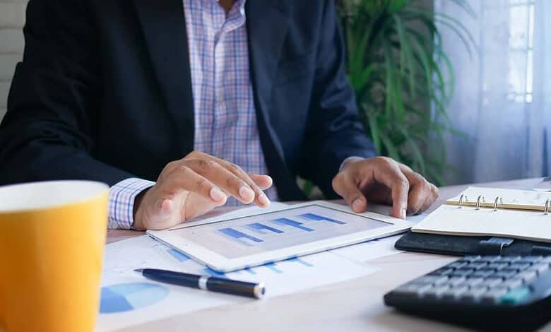 Business professional using tablet and documents for running insights analysis, calculator and notebook on desk.