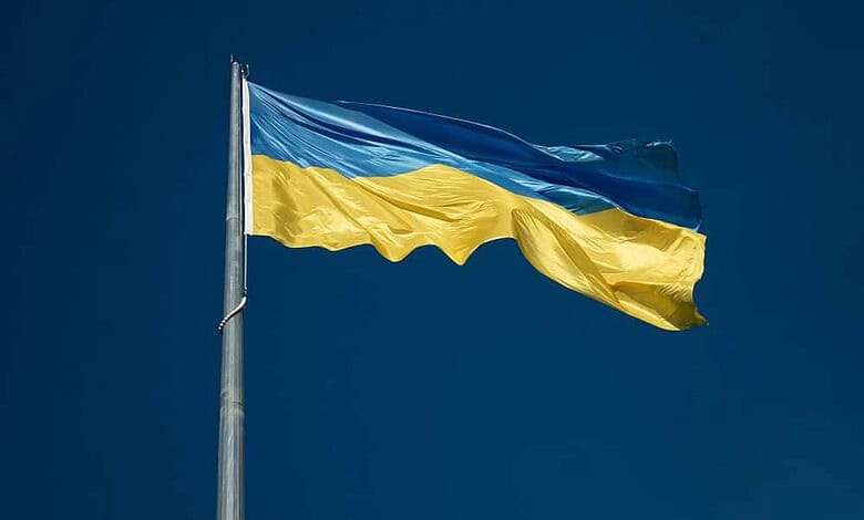 Ukrainian flag waving on a tall flagpole against a clear blue sky, symbolizing national pride and resilience.