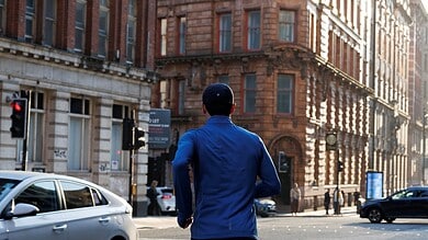 Male runner in blue jacket and black shorts running through city streets with historic buildings in the background.