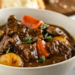 Bowl of beef stew with chunks of beef, carrots, and potatoes. Garnished with fresh thyme leaves
