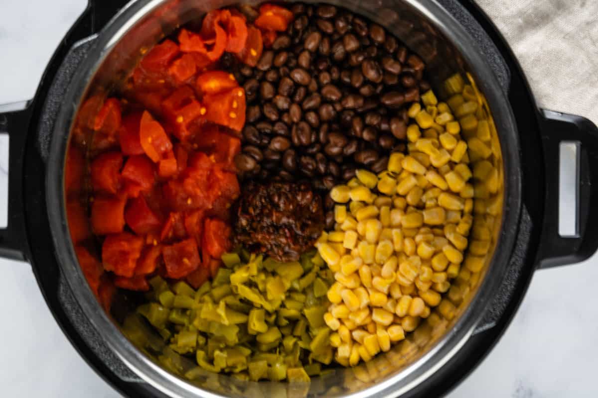 Ingredients in an Instant Pot: diced tomatoes, black beans, corn, diced green chilies and chipotle in adobo paste.