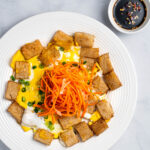 A plate of bot chien with pickled carrots and daikon on top and dipping sauce on the side.
