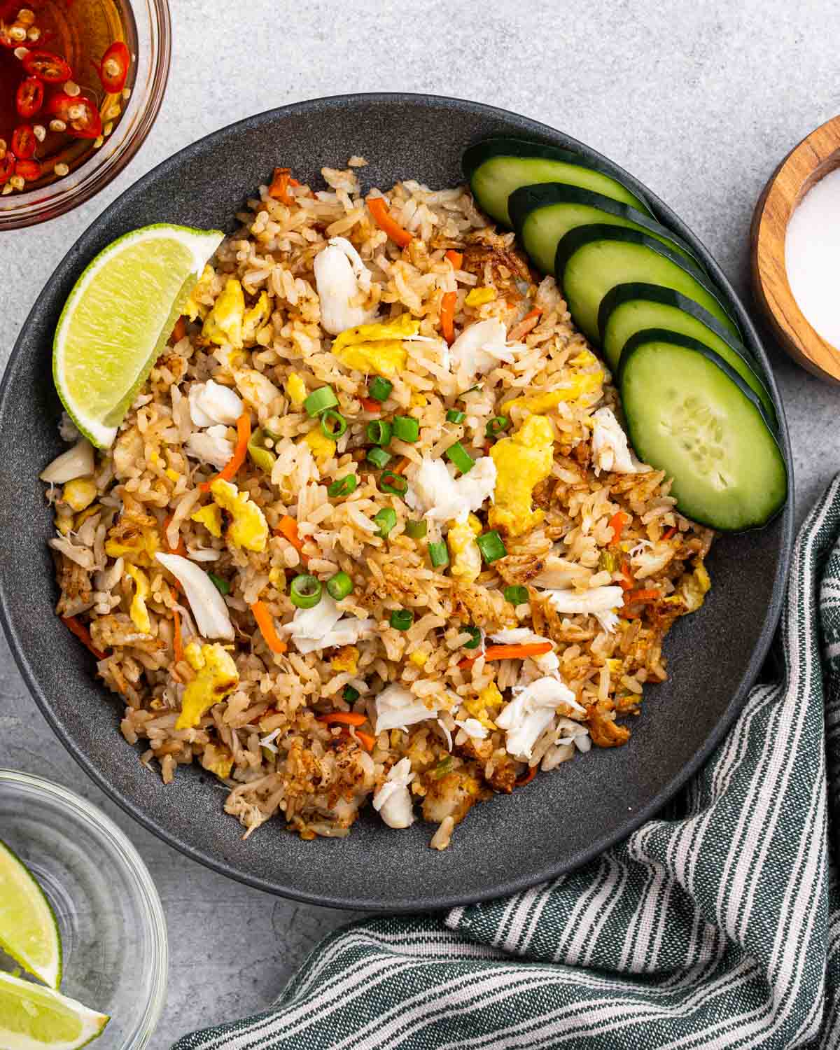 Plate of crab fried rice with side of lime wedges, sliced cucumbers and spicy fish sauce.