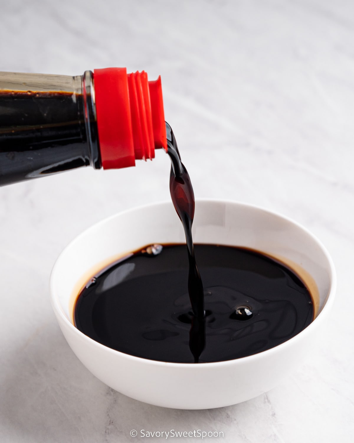 Bottle of dark soy sauce pouring into bowl.