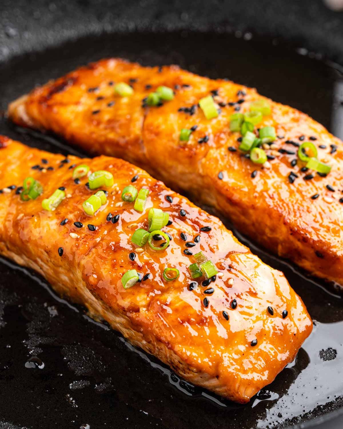 Slices of miso salmon on a pan topped with sesame seeds and green onions.