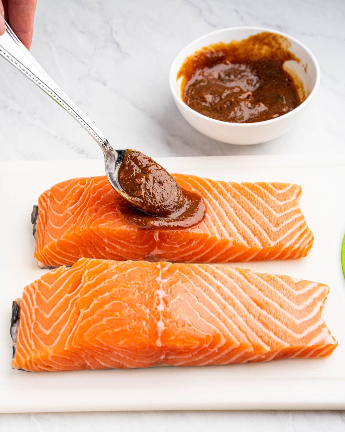 Spoon pouring miso sauce on the salmon.