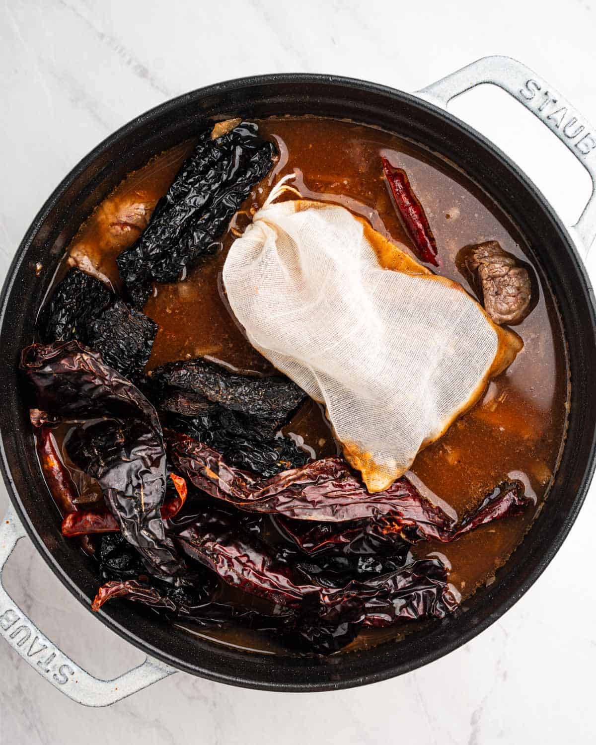 Pot of broth, dried chilies, spices, and beef.