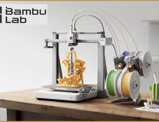 Bambu Lab A2L 3D printer printing a gold model beside multicolour filament spools