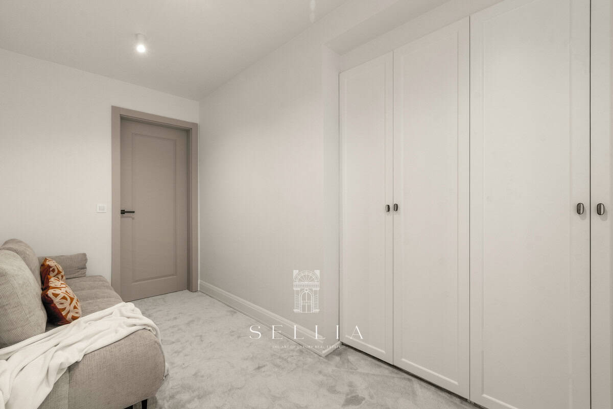 Przestronny, jasny pokój z białymi szafami i szarą sofą w luksusowym penthousie.