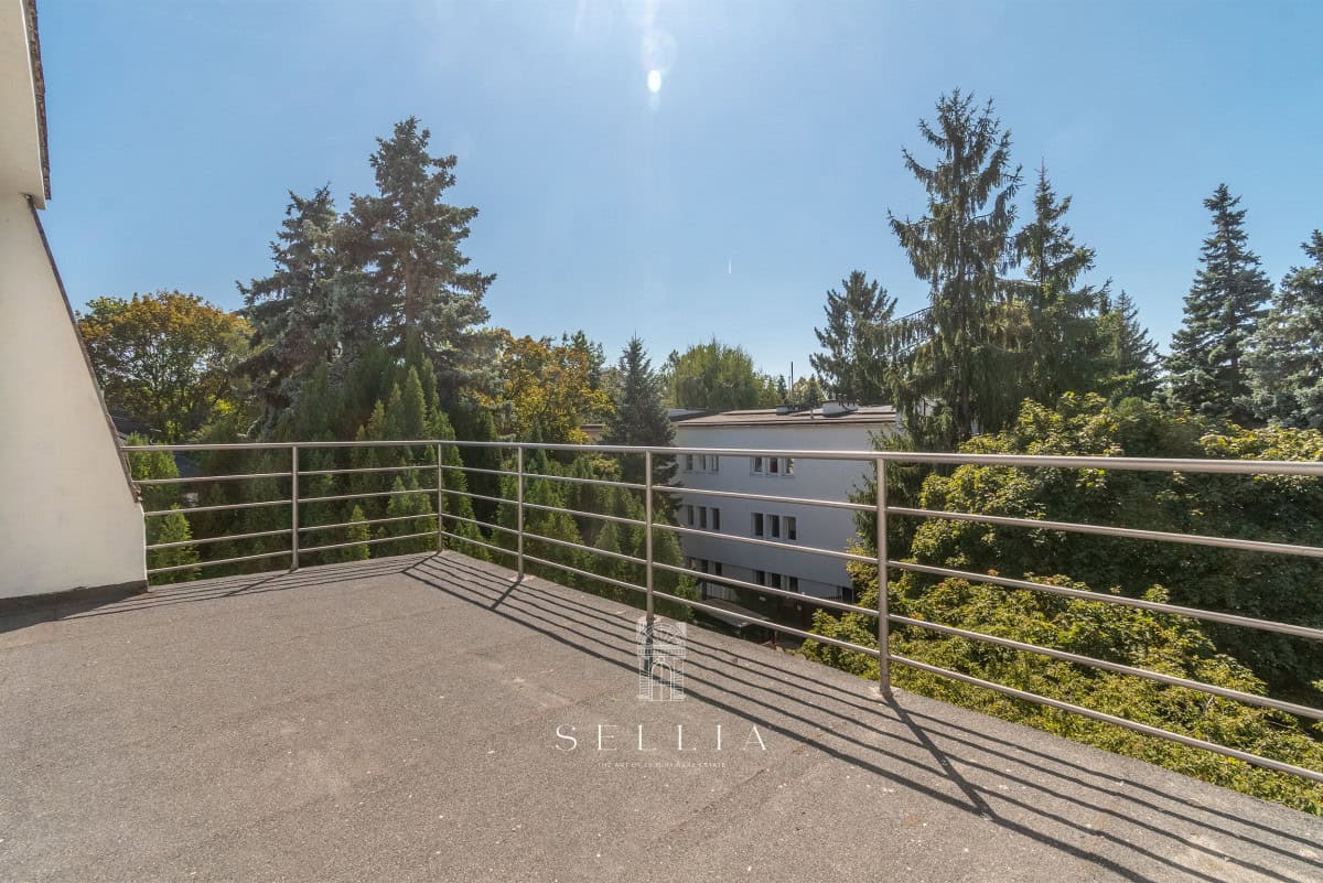 Taras z metalowym balustradą, otoczony zielonymi drzewami i niebem.