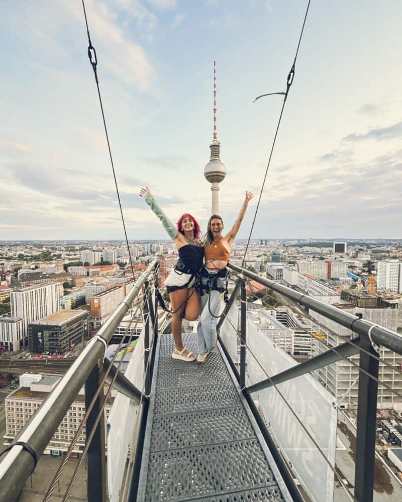 Two women on a glass skywalk with Berlin TV Tower in the background.