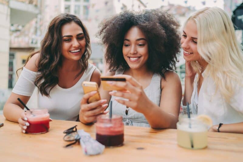 Group of young women enjoying drinks and chatting at Flying Pig Uptown Hostel outdoor terrace.