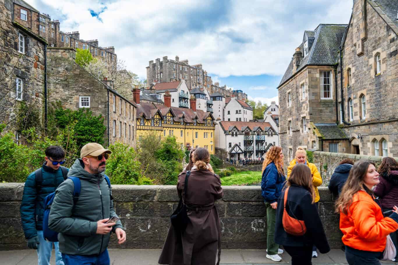Tourists on a bridge with historic stone buildings and castle in the background. at St Christopher's Edinburgh Old Town hostel