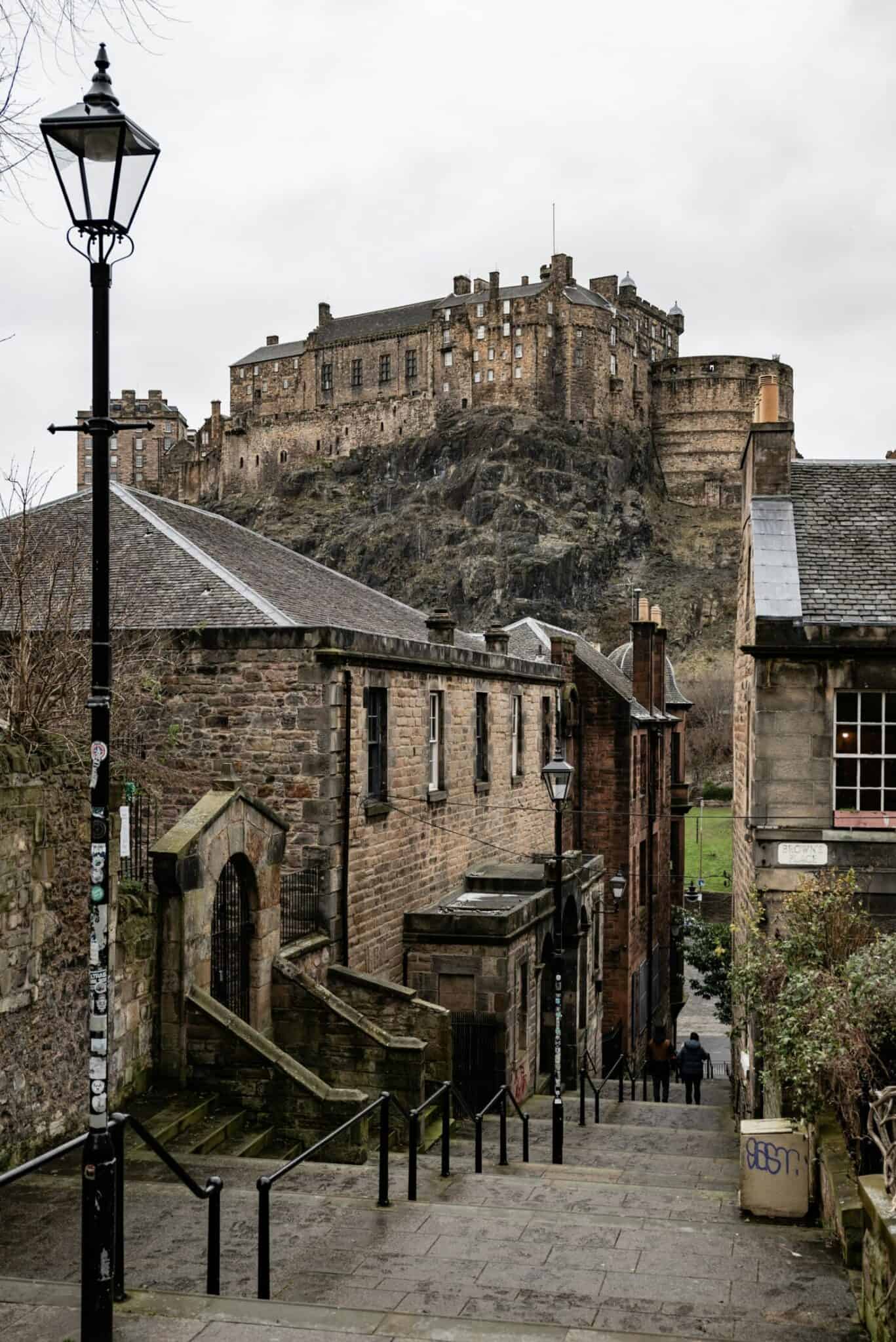 Street view with stone buildings and castle in the background, lamppost and cobbled path. at St Christopher's Edinburgh Old Town hostel