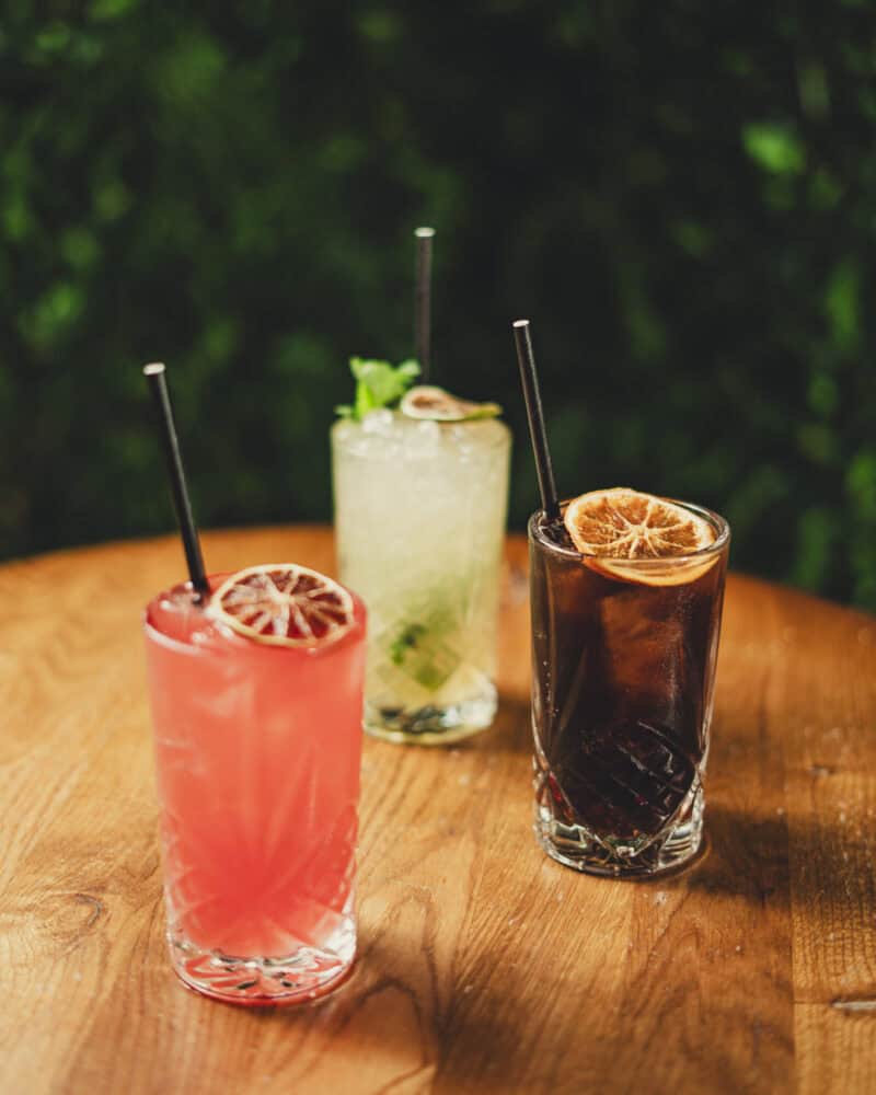 A selection of colourful cocktails on a wooden table in a social bar setting.