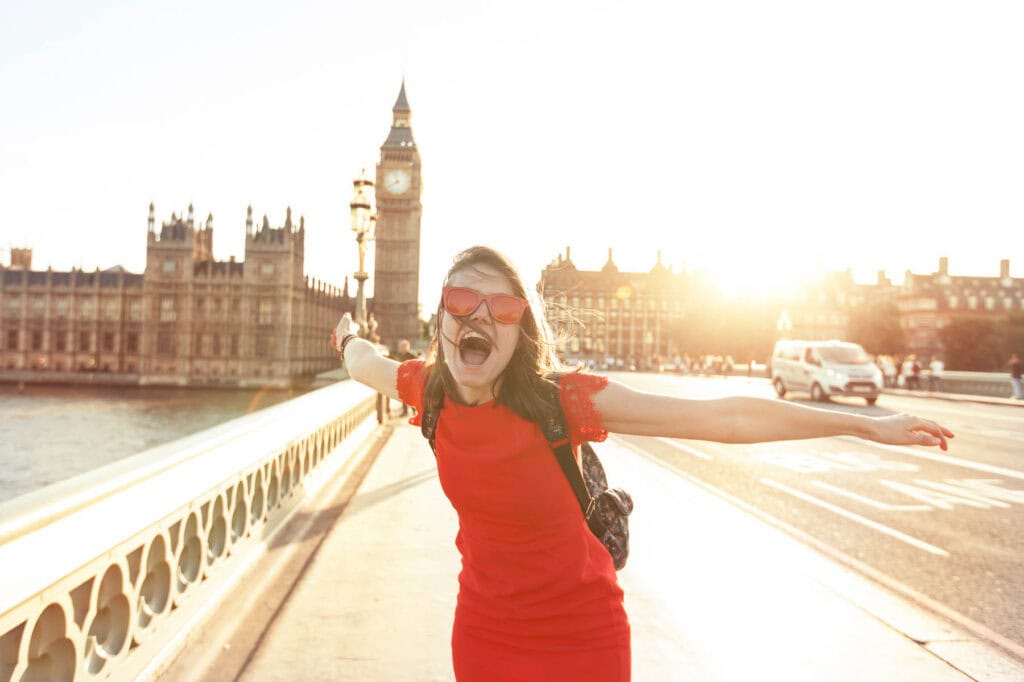 London sightseeing at sunset with Big Ben in the background and a joyful woman in a red dress.