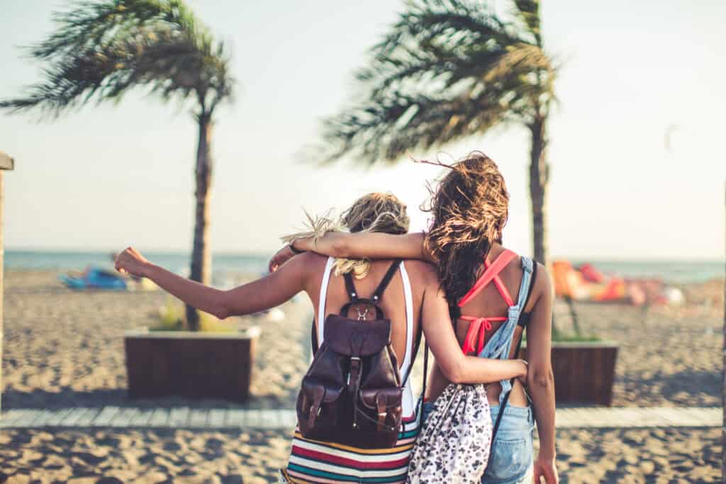 Relaxed women with backpacks walking along the beach promenade.