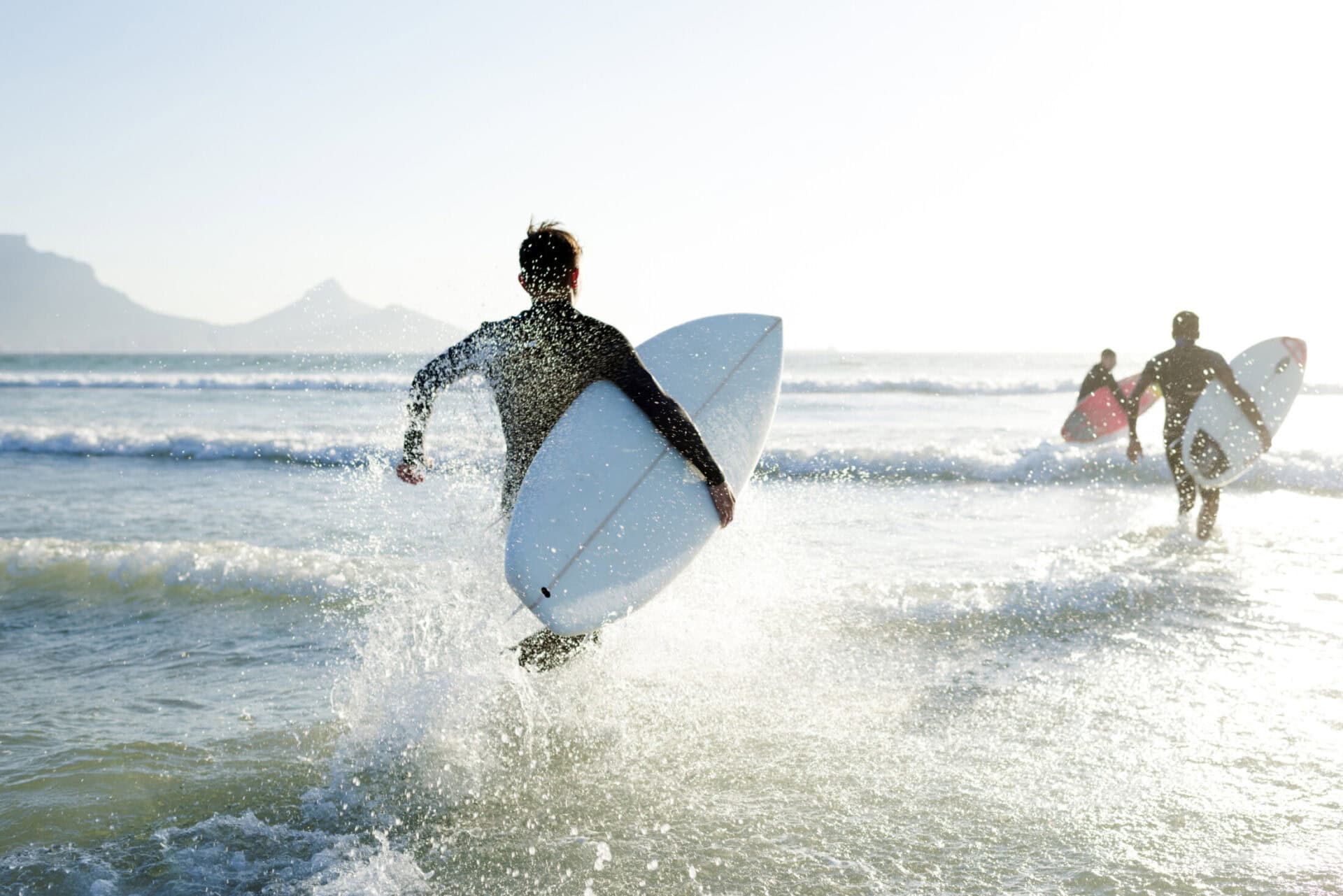 Group of surfers running into the sea with surfboards at sunset in Berlin.