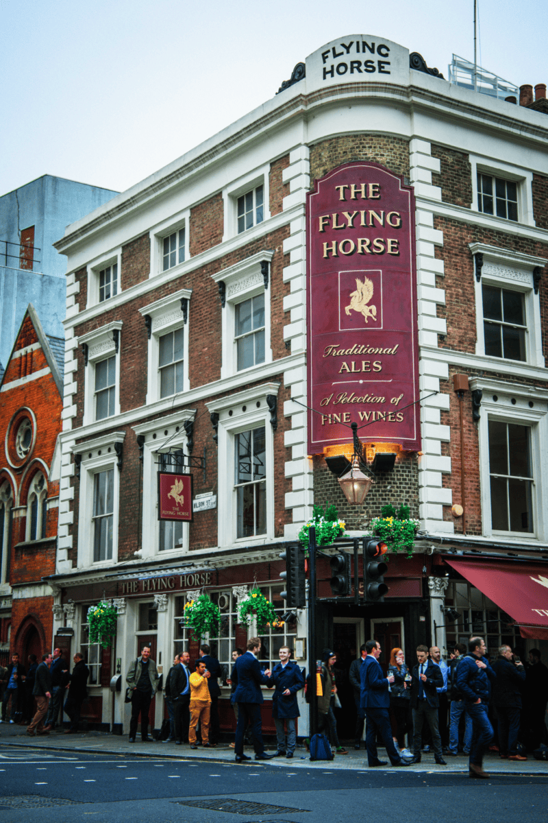 A traditional pub on a busy street corner with a sign for ales and wines.