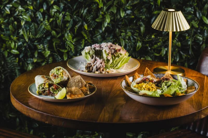 A variety of vegan dishes served on a wooden table in a social hostel setting.