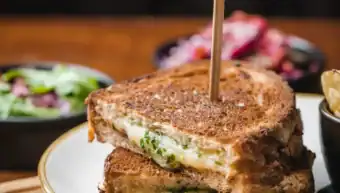 Close-up of a grilled cheese sandwich with melted cheese and herbs.