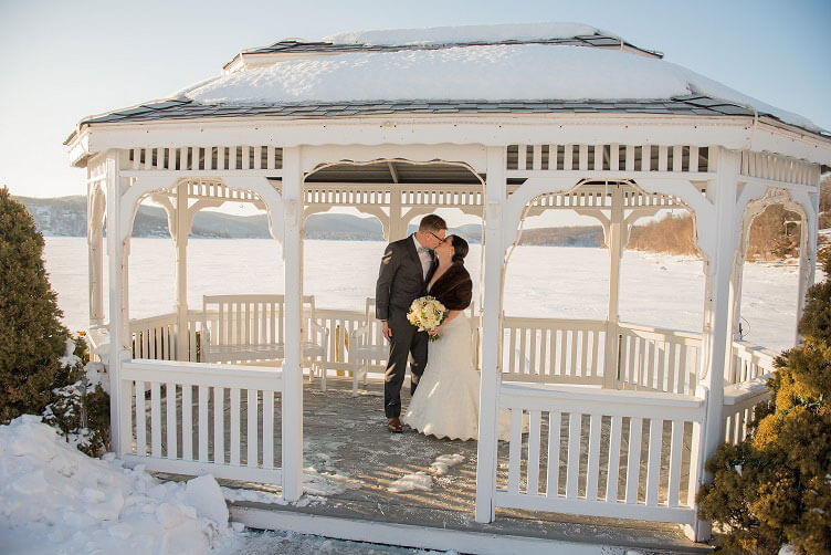 Bride and groom share a winter wedding kiss in the lakeside gazebo at Candlewood Inn.
