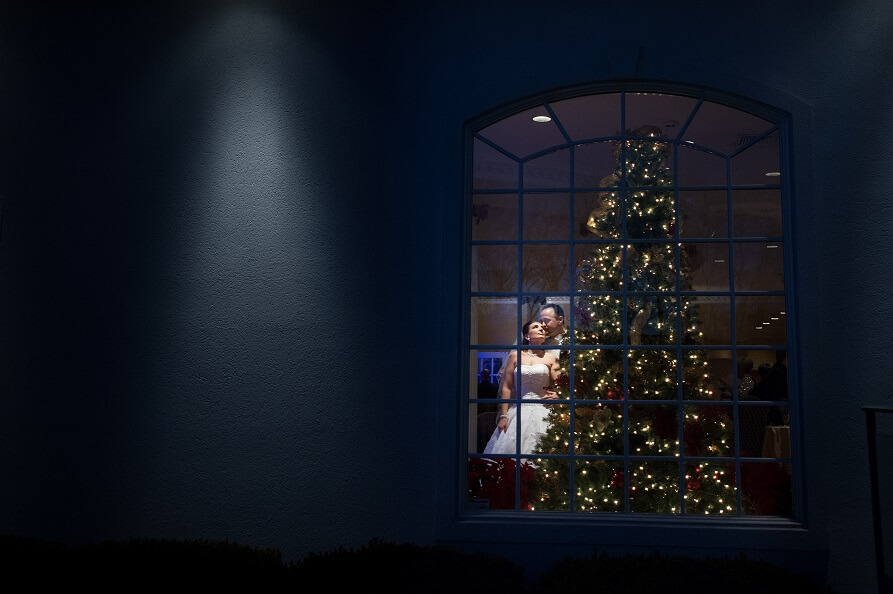 Melissa and Manny's Wedding Day portrait by a Christmas tree, viewed through a window at night.