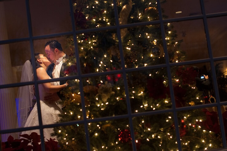Melissa and Manny's wedding day kiss beside a glowing holiday tree at Candlewood Inn.