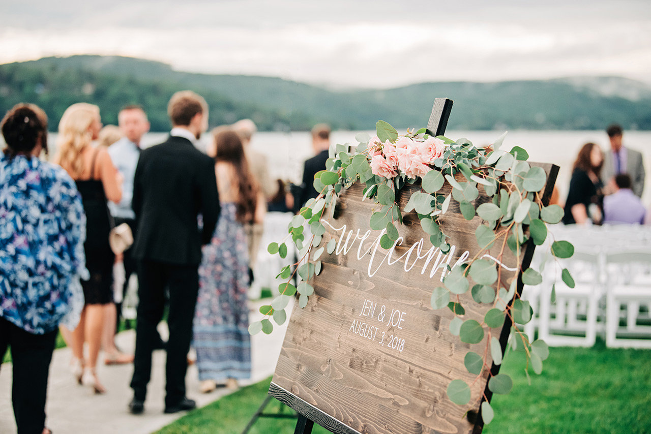 Rustic welcome sign with floral accents at a lakeside wedding ceremony at Candlewood Inn.