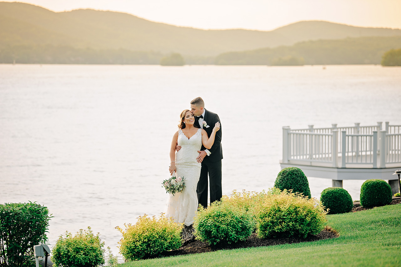 Bride and groom pose by the lake at sunset during a Candlewood Inn waterfront wedding.