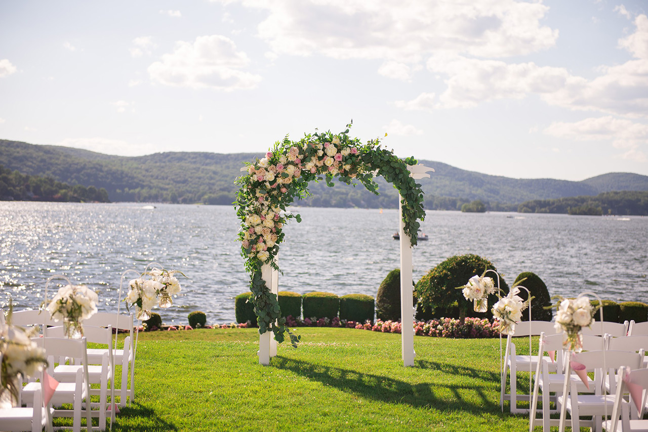 Floral wedding arch overlooking a scenic lake, set for an elegant outdoor ceremony.