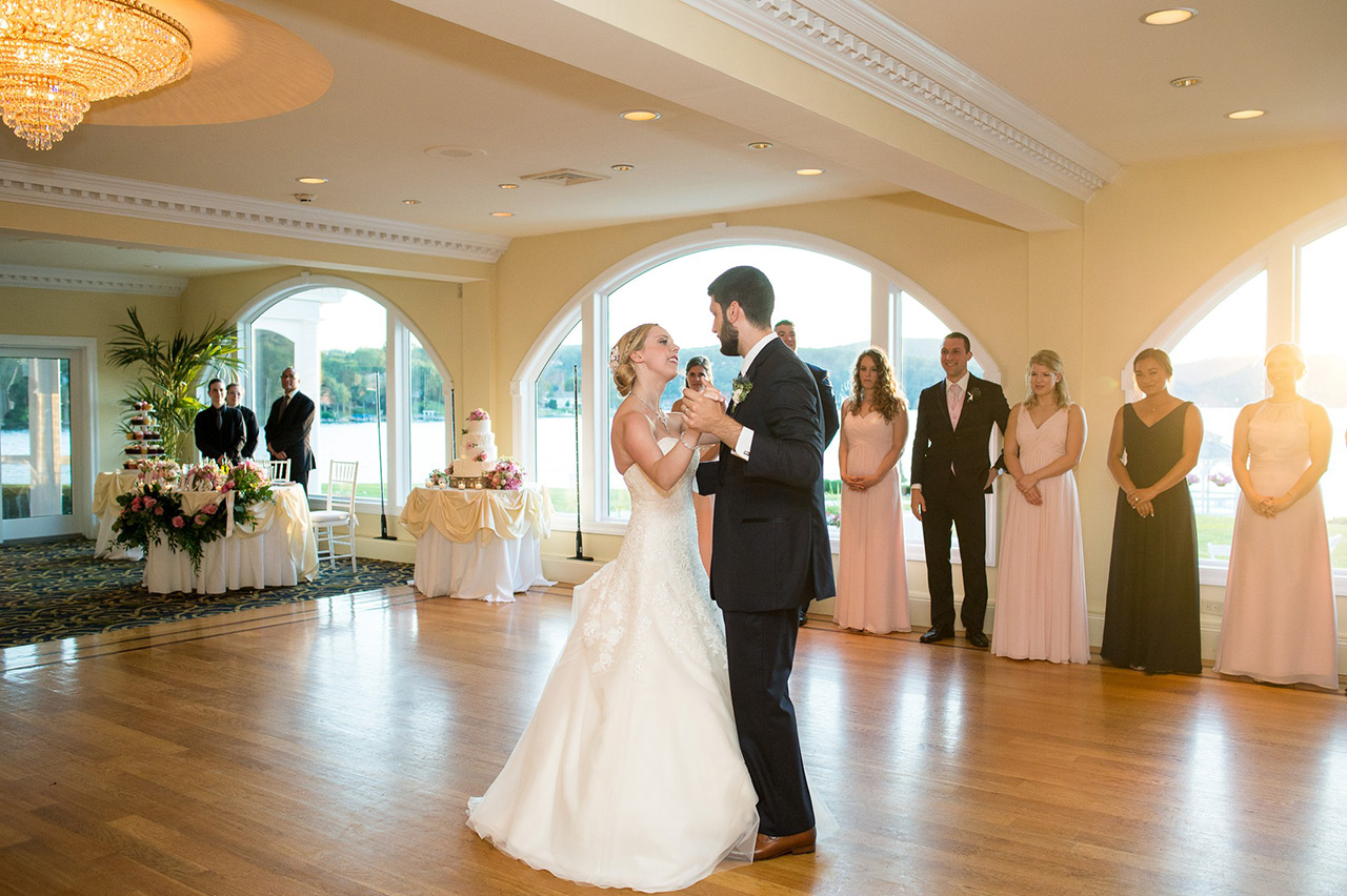 Bride and groom share their first dance in an elegant ballroom surrounded by wedding guests.