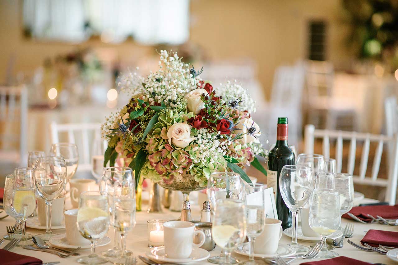 Wedding reception table with elegant floral centerpiece, candles, and formal place settings.