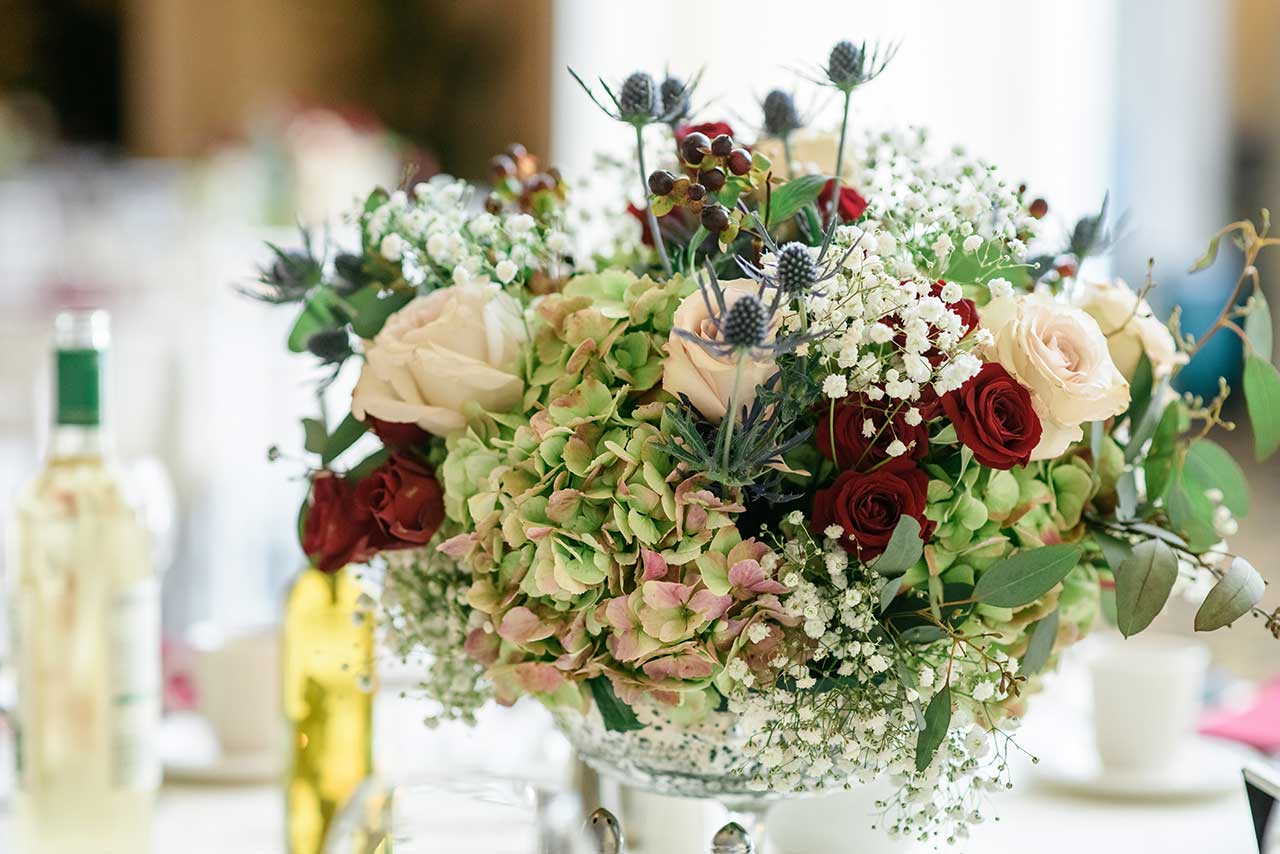 Elegant wedding centerpiece with roses, hydrangeas, baby's breath, and greenery.