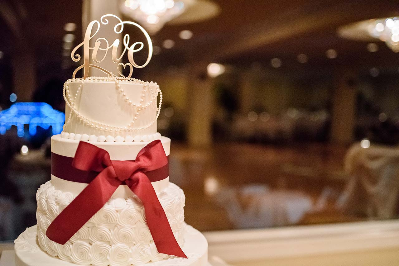 Elegant wedding cake with pearl details and red ribbon at Candlewood Inn reception.