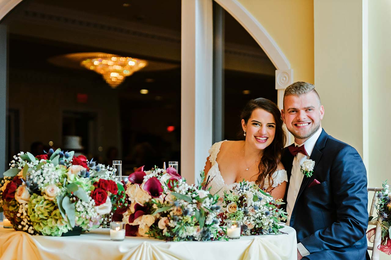 Bride and groom seated at their sweetheart table with floral arrangements at Candlewood Inn.
