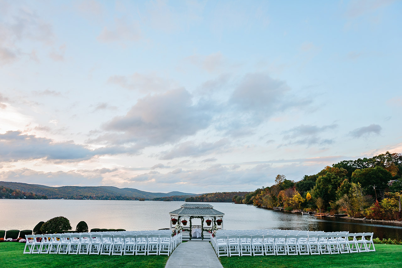 Lakeside wedding ceremony with white chairs and gazebo overlooking the water.